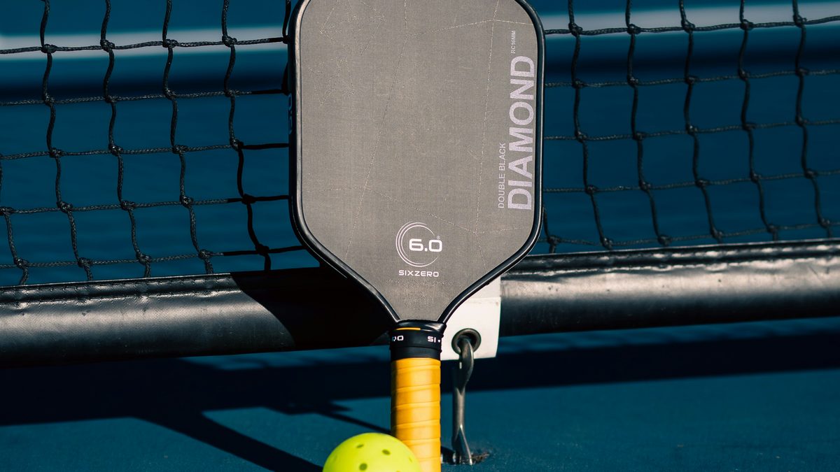 A pickleball paddle and ball resting against the net on a blue court